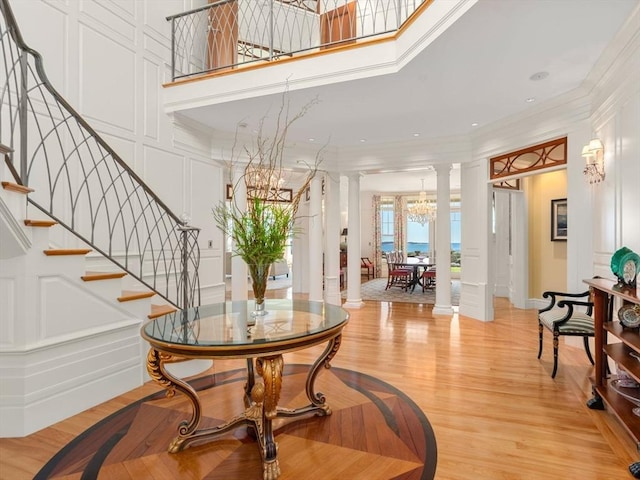 foyer featuring stairway, an inviting chandelier, ornamental molding, and ornate columns
