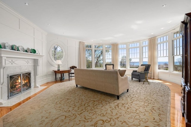 living room with a decorative wall, wood finished floors, a premium fireplace, ornamental molding, and recessed lighting