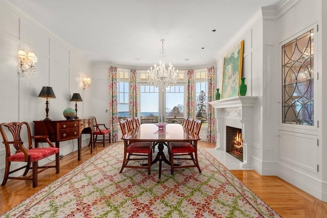 dining room with a fireplace with flush hearth, a decorative wall, crown molding, and an inviting chandelier