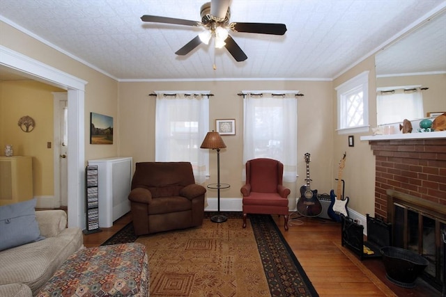 living room featuring a brick fireplace, hardwood / wood-style flooring, ornamental molding, and ceiling fan