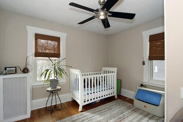 bedroom featuring a nursery area, ceiling fan, baseboards, and wood finished floors