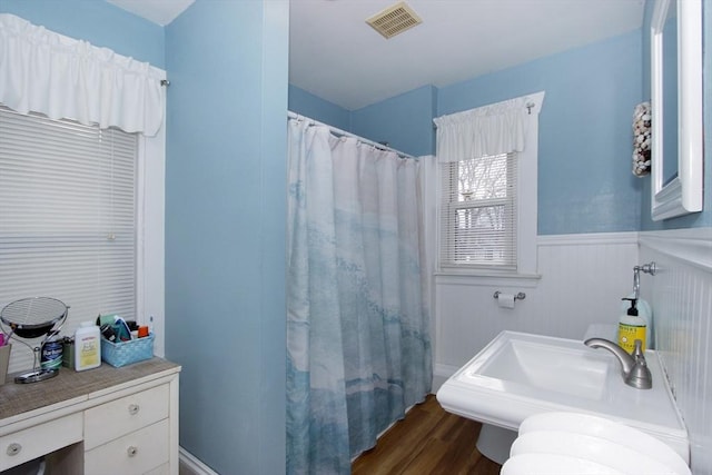 full bathroom with visible vents, curtained shower, wainscoting, wood finished floors, and a sink