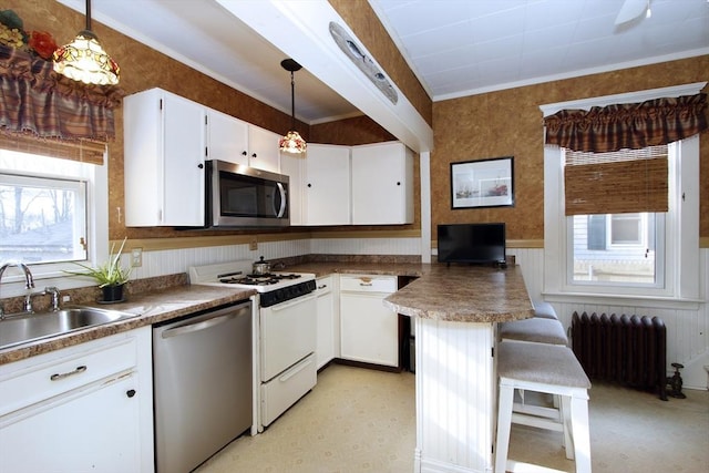 kitchen with a sink, radiator, appliances with stainless steel finishes, white cabinets, and wallpapered walls