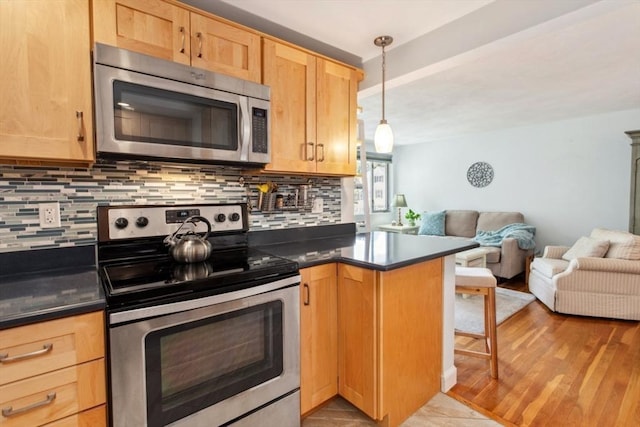 kitchen featuring appliances with stainless steel finishes, open floor plan, dark countertops, tasteful backsplash, and a peninsula