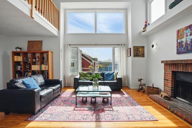 living room featuring a fireplace, a towering ceiling, baseboards, and wood finished floors
