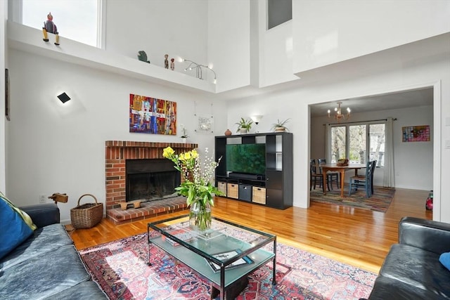 living room featuring a towering ceiling, a chandelier, wood finished floors, and a fireplace