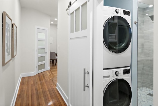 clothes washing area with stacked washer / dryer, a barn door, hardwood / wood-style floors, baseboards, and recessed lighting