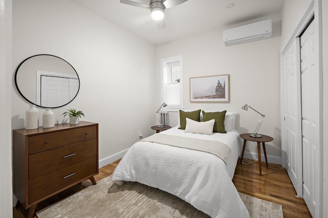 bedroom with wood finished floors, a closet, a wall mounted air conditioner, baseboards, and a ceiling fan