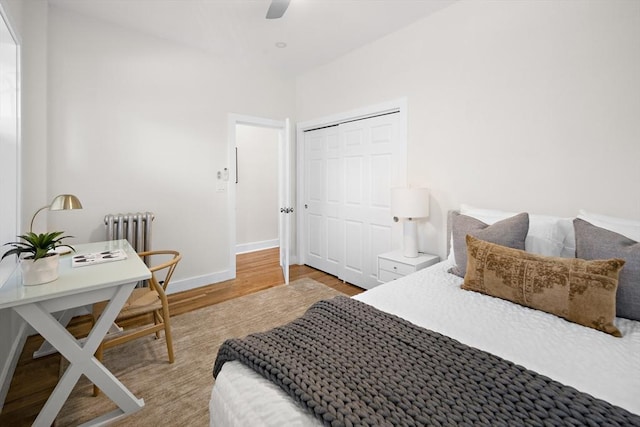 bedroom with a closet, ceiling fan, radiator heating unit, baseboards, and wood finished floors