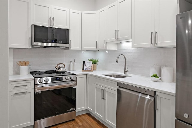 kitchen featuring light stone counters, appliances with stainless steel finishes, white cabinets, a sink, and light wood-type flooring