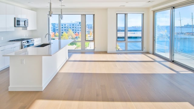 kitchen featuring appliances with stainless steel finishes, hanging light fixtures, white cabinetry, light hardwood / wood-style floors, and a kitchen island with sink