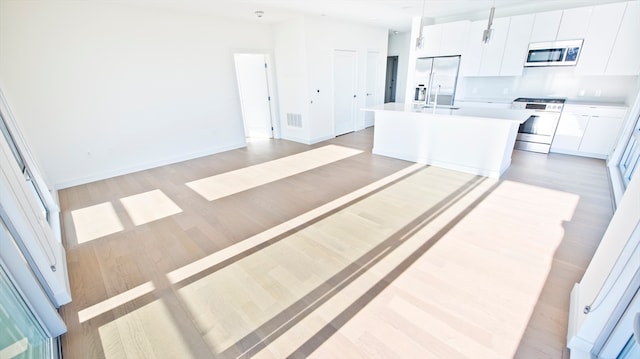 kitchen featuring light wood-type flooring, white cabinetry, stainless steel appliances, decorative light fixtures, and a kitchen island with sink