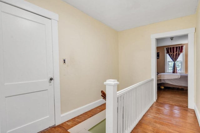corridor featuring baseboards, an upstairs landing, and light wood-style flooring