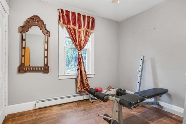 workout room featuring a baseboard heating unit, baseboards, and wood finished floors