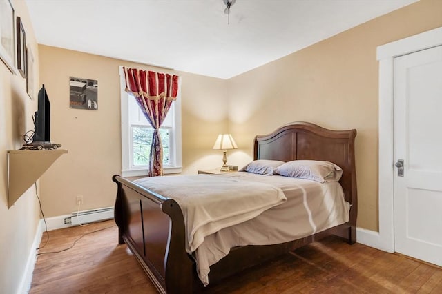 bedroom with baseboard heating, wood finished floors, and baseboards