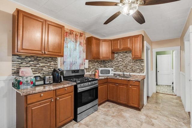 kitchen with stainless steel range with gas cooktop, brown cabinets, white microwave, and ceiling fan