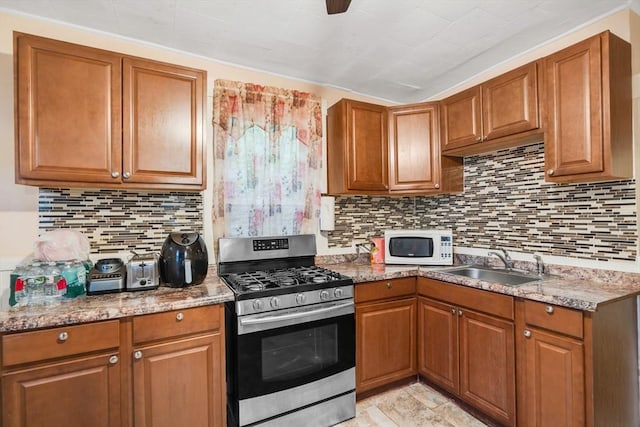 kitchen featuring gas range, brown cabinetry, a sink, and white microwave