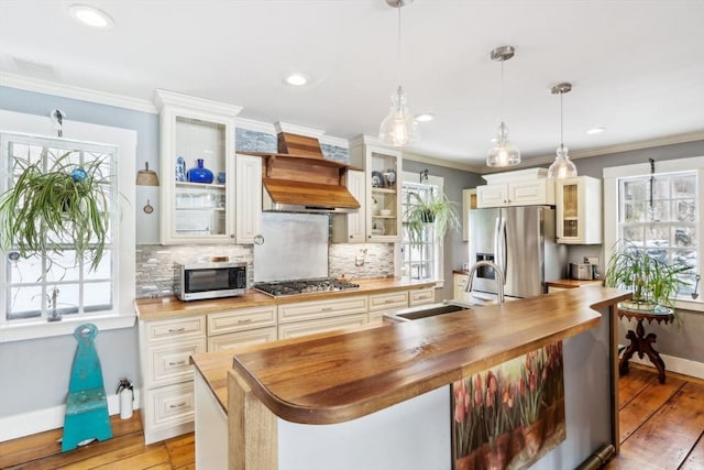 kitchen with sink, wooden counters, hanging light fixtures, stainless steel appliances, and light hardwood / wood-style flooring