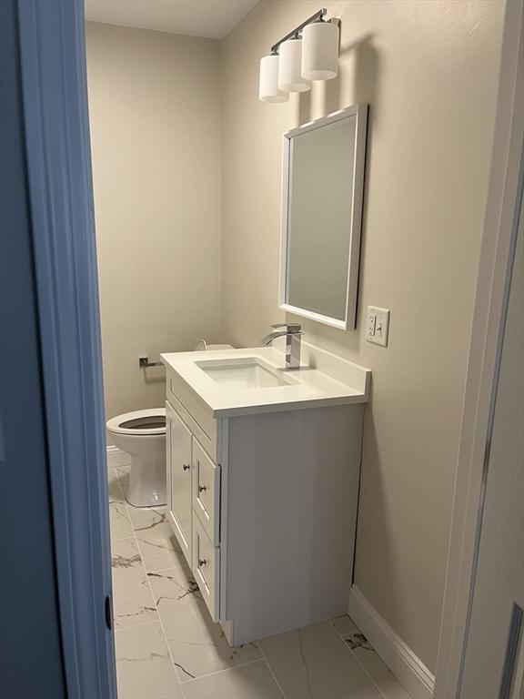 bathroom featuring marble finish floor, baseboards, vanity, and toilet