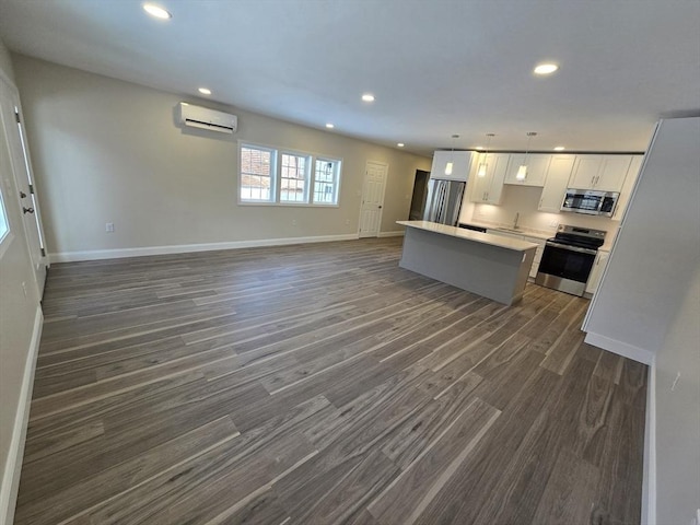 kitchen with a wall unit AC, appliances with stainless steel finishes, open floor plan, a center island, and recessed lighting