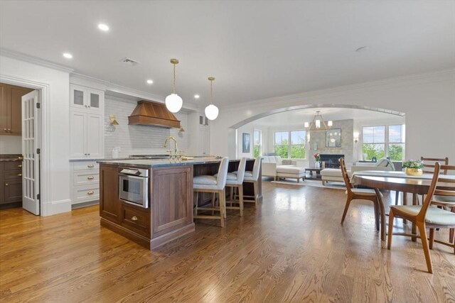 197-199 Winchester St, Brookline, MA 02446 - kitchen featuring custom range hood, a glass covered fireplace, arched walkways, ornamental molding, and light wood-style floors