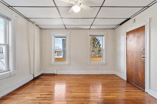 empty room with a wealth of natural light, light hardwood / wood-style floors, a drop ceiling, and a baseboard heating unit