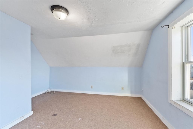 bonus room featuring a healthy amount of sunlight, vaulted ceiling, carpet, and a textured ceiling