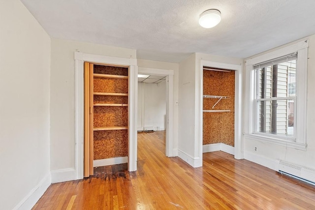 unfurnished bedroom featuring a baseboard heating unit, a textured ceiling, light wood-type flooring, and a closet