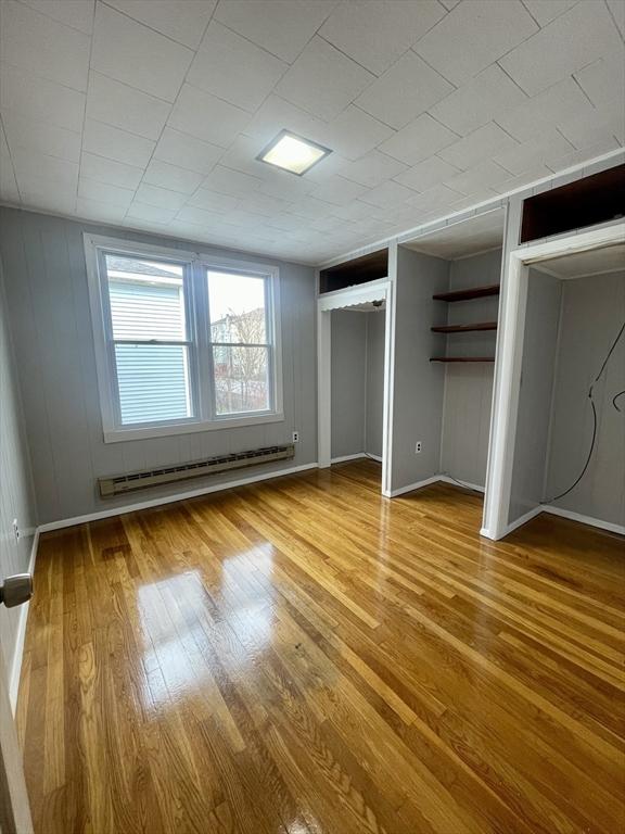 unfurnished bedroom with baseboards, a baseboard radiator, multiple closets, and light wood-style flooring