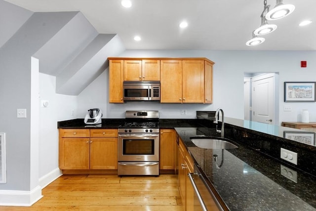kitchen with stainless steel appliances, a sink, light wood-style floors, dark stone counters, and recessed lighting