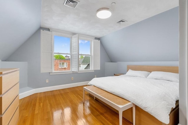 bedroom featuring baseboards, light wood finished floors, and lofted ceiling
