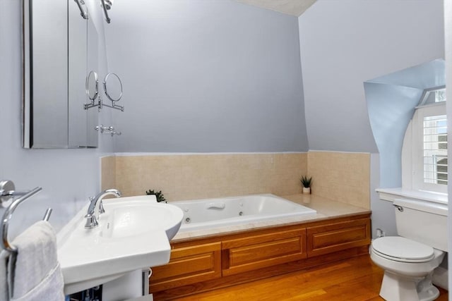 bathroom with a jetted tub, toilet, wood finished floors, and a sink