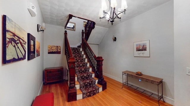 staircase with a chandelier, wood finished floors, baseboards, and vaulted ceiling