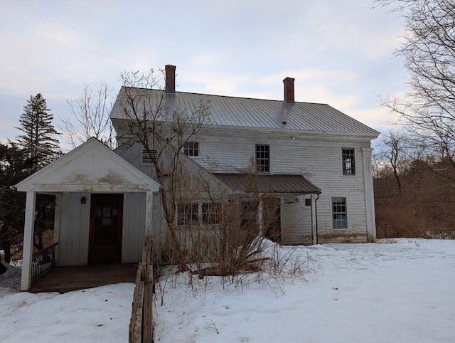 snow covered property featuring metal roof and a chimney