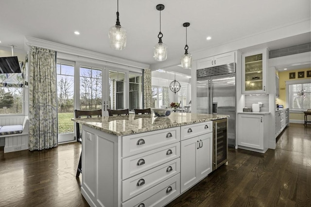 kitchen with built in fridge, decorative light fixtures, wine cooler, white cabinets, and a center island