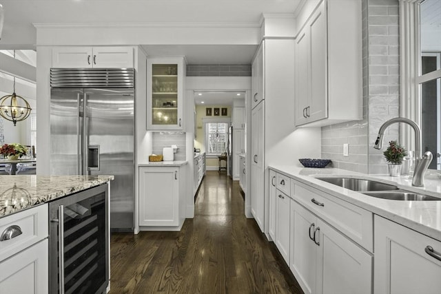 kitchen featuring sink, built in refrigerator, wine cooler, light stone countertops, and white cabinets