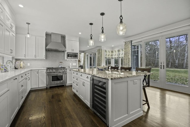 kitchen featuring appliances with stainless steel finishes, wine cooler, a kitchen island, decorative light fixtures, and wall chimney exhaust hood