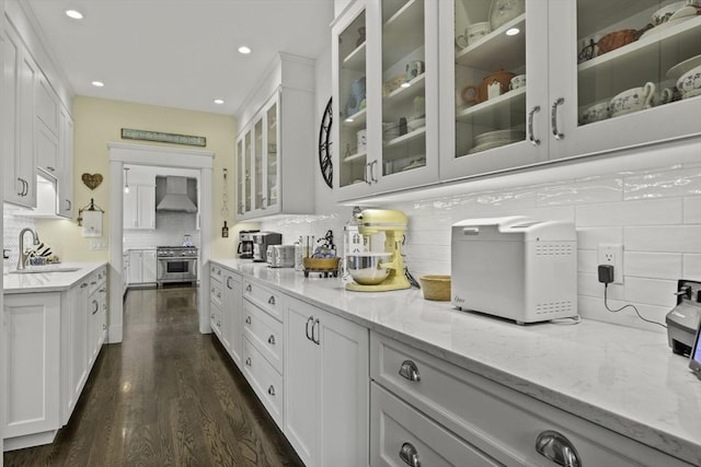 interior space featuring white cabinetry, sink, wall chimney range hood, and high end stainless steel range