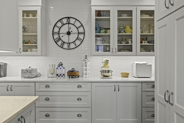 bar with light stone counters, decorative backsplash, and white cabinets