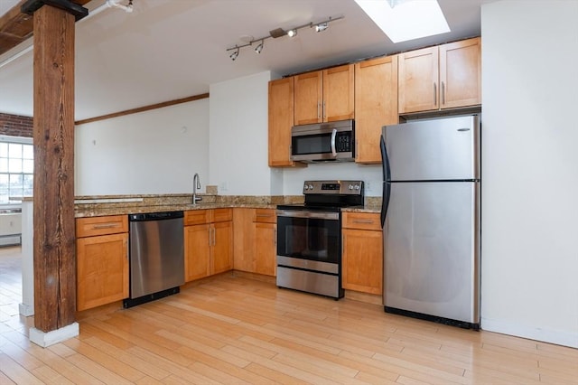 kitchen featuring light stone countertops, stainless steel appliances, a skylight, and light wood-style flooring