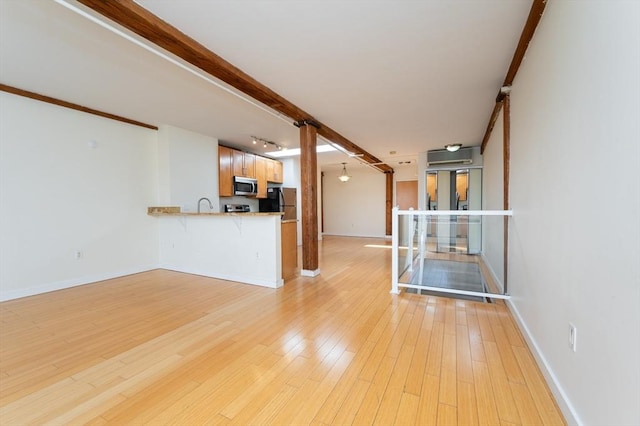 unfurnished living room featuring light wood finished floors, baseboards, a sink, and a wall unit AC