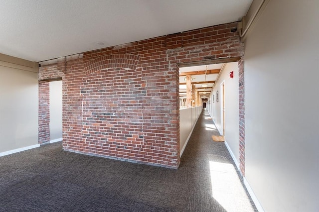 corridor featuring brick wall, carpet floors, and baseboards