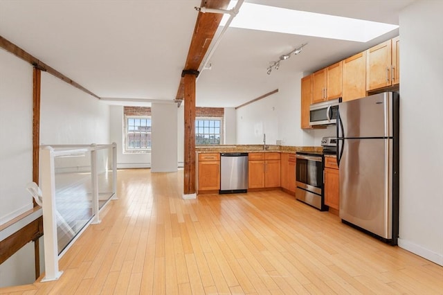 kitchen with a sink, baseboards, light wood-style floors, track lighting, and appliances with stainless steel finishes