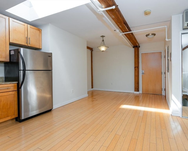 kitchen featuring a skylight, baseboards, freestanding refrigerator, and light wood finished floors