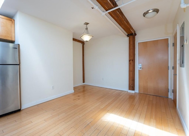 empty room with light wood-style flooring, baseboards, and beam ceiling