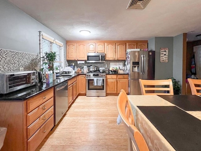 kitchen featuring appliances with stainless steel finishes, sink, dark stone countertops, decorative backsplash, and light wood-type flooring