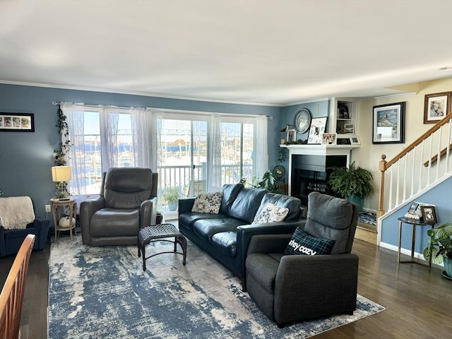 living room featuring stairs, ornamental molding, plenty of natural light, wood finished floors, and a fireplace