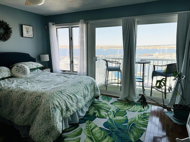 bedroom featuring a water view, wood finished floors, access to exterior, and a textured ceiling