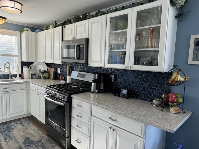 kitchen with stainless steel appliances, white cabinets, a sink, decorative backsplash, and glass insert cabinets