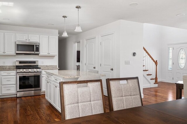 kitchen featuring white cabinetry, light stone counters, dark wood finished floors, hanging light fixtures, and stainless steel appliances